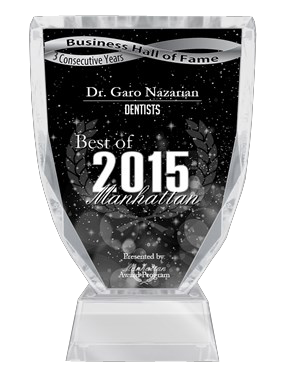 The image shows a clear glass award plaque with text indicating recognition for Best of Manhattan Dentist 2015 and the name Dr. Gano Nazarian. The plaque also includes a laurel wreath symbol, and there is a black background with white stars above the plaque.